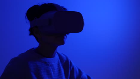 young teenager wearing vr augmented reality goggles dancing in blue room