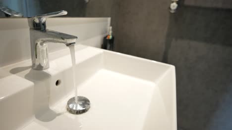 close up of a white bathroom sink with a stainless steel faucet running water