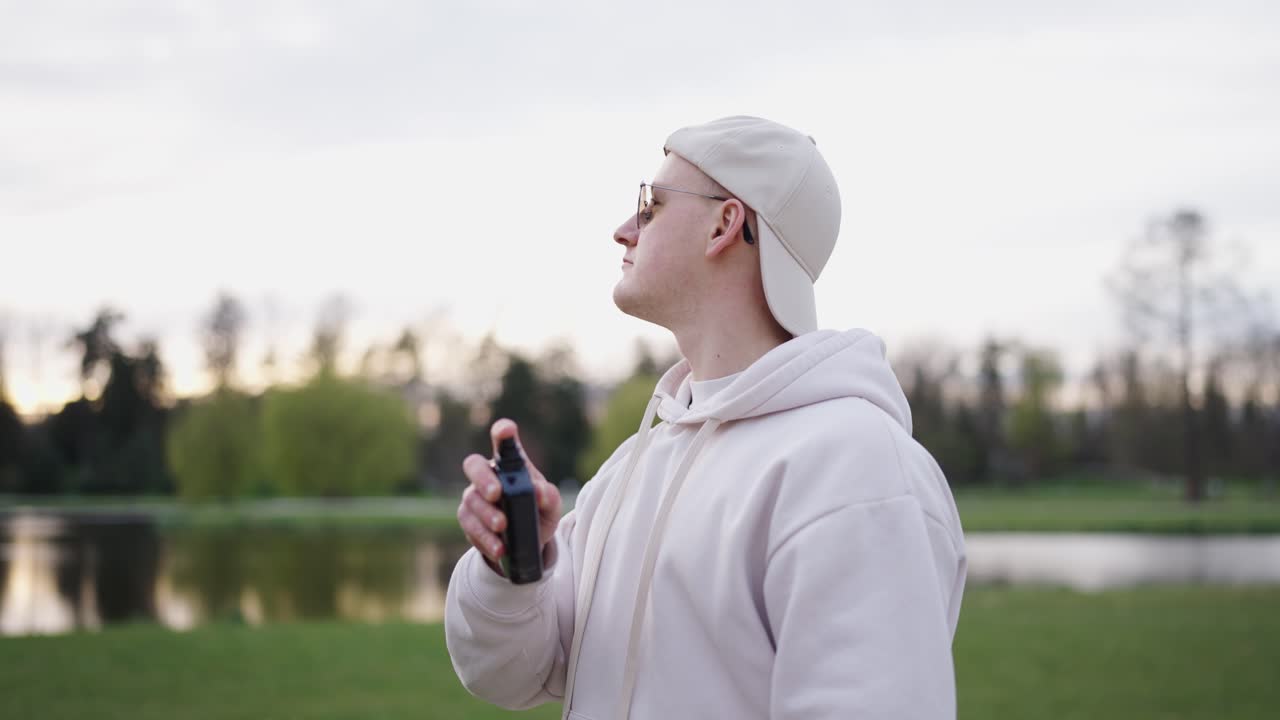 Confident male with sunglasses spray perfume under neck and on clothes
