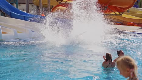 Happy people in the water park. Young woman sliding down into the blue water of the pool. Beautiful water splashes outdoors. Slow motion.