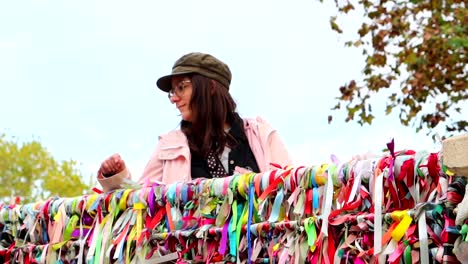 Woman-wearing-hat-and-glasses-at-the-bridge-of-friendship-covered-in-colorful-ribbons-in-Aveiro,-Portugal