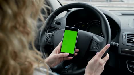 mujer se sienta en el coche moderno y trabaja en el teléfono inteligente - manos de primer plano. pantalla verde. llave croma