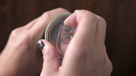 female hand opening beer can on wooden table in restaurant