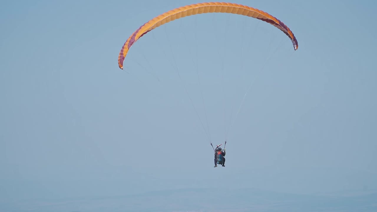 A stunning aerial scene featuring three paragliders soaring across an open sky. Their vibrant purple, green, and red parachutes stand out.