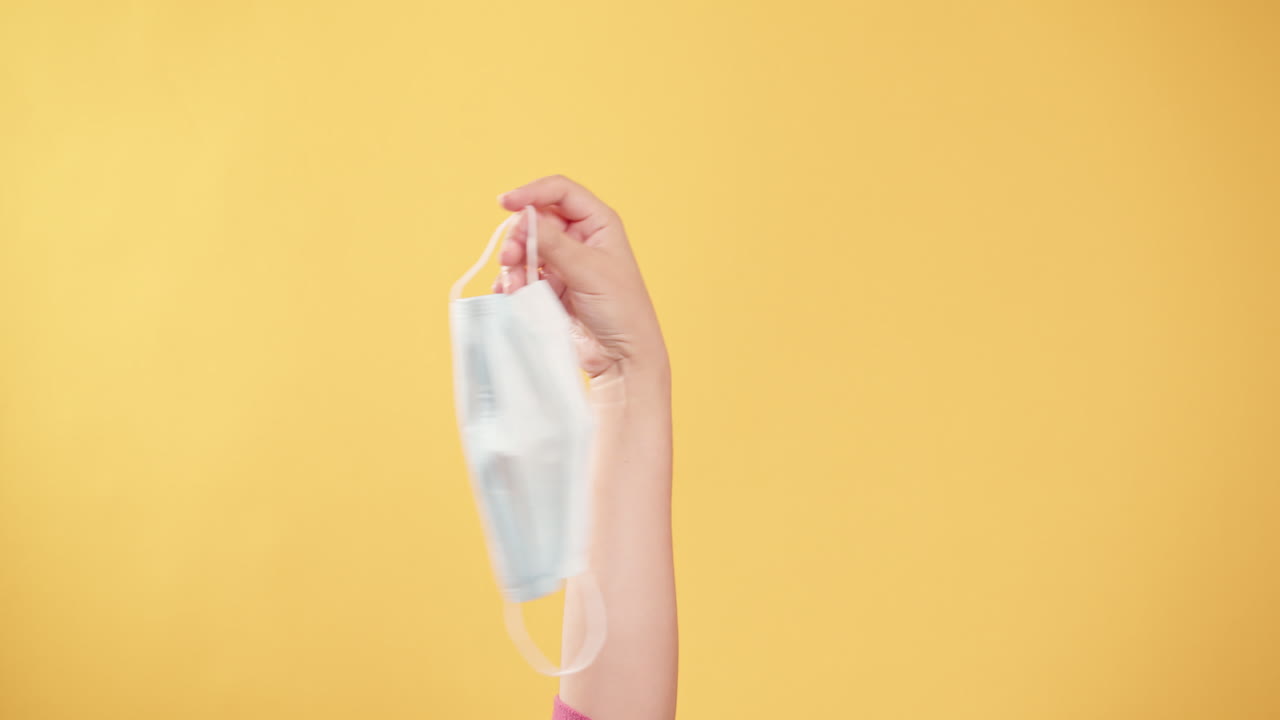 mano sosteniendo la máscara protectora y quitándosela para tomar aire fresco después de que la situación de civid-19 se deshaga con el fondo amarillo-1