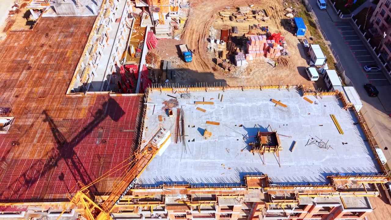 Elevated perspective of a leveled building top with materials, bricks, and a crane shadow on the ground. High angle view of concrete roof slab under construction.