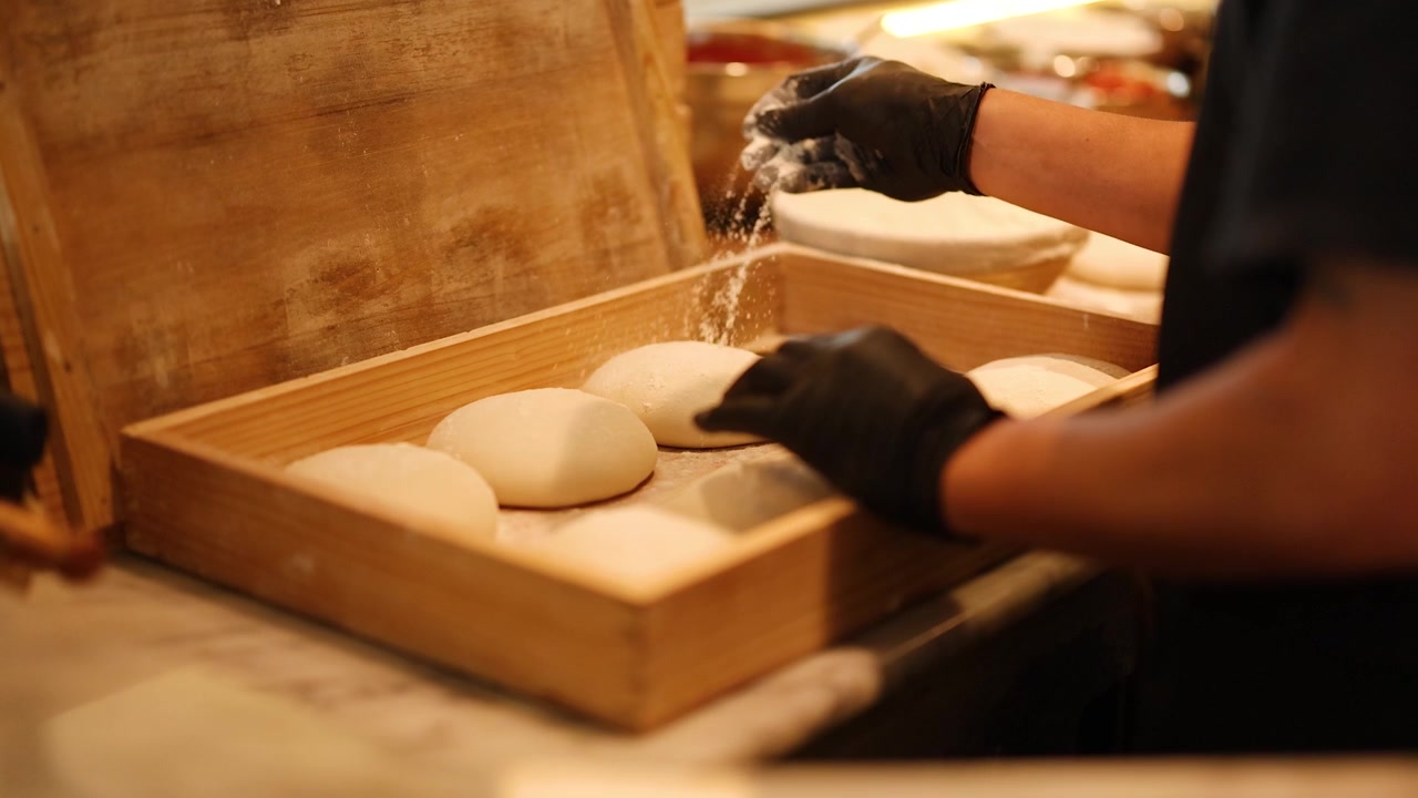Pizzaiolo con guanti neri infarina palline di impasto fresco per pizza in una cassa di legno