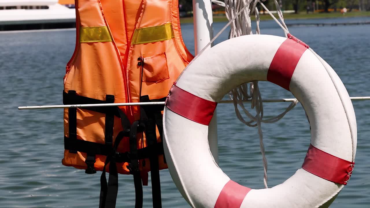 Close-up of life jackets and a lifebuoy ring beside a calm waterfront.