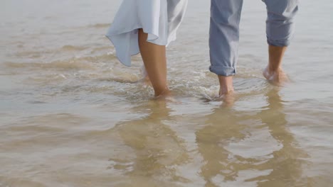 pies de cerca de una joven pareja caucásica caminando en la orilla del mar.