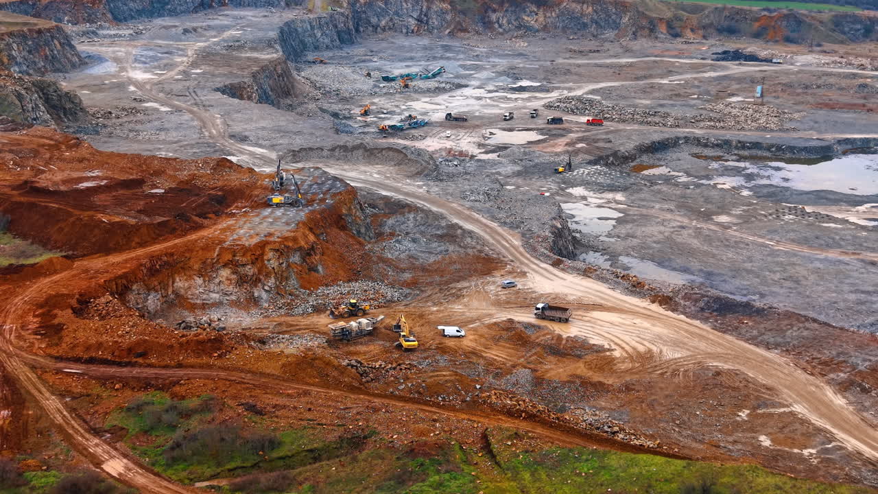 Wide panoramic aerial view of active open pit granite quarry. High angle landscape shot of a large scale industrial mining operation with multiple levels and machinery