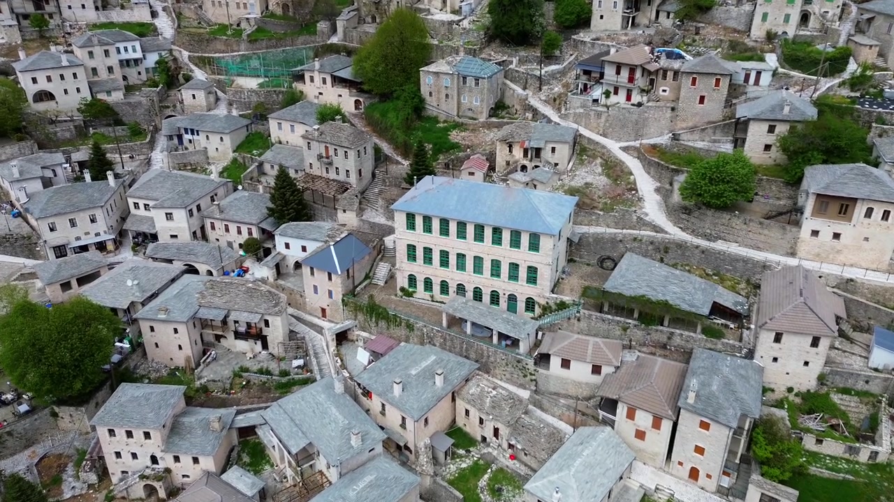 Inquadratura cinematografica 4K con drone in avvicinamento verso l'iconico edificio scolastico storico in pietra a Syrrako. Vista aerea di tetti tradizionali in ardesia e architettura regionale dell'Epiro in Grecia