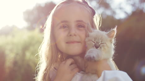 retrato de una niña rubia sosteniendo un gatito y sonriendo a la luz del sol