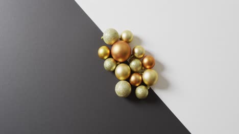 Video-of-glittery,-gold-and-bronze-baubles-on-black-and-white,-with-copy-space