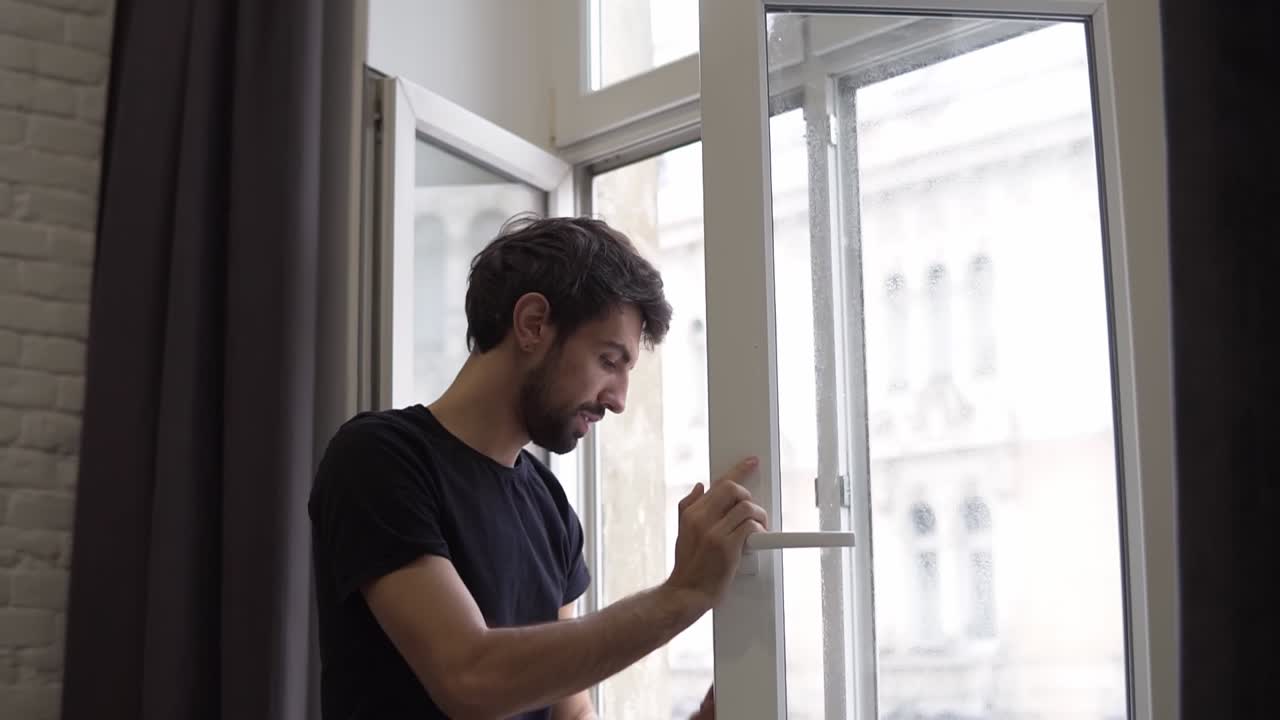 el hombre está limpiando la ventana, limpiando la superficie y usa un trapo, de pie en un apartamento moderno