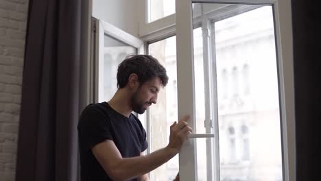 man is cleaning window, cleans surface and uses a rag, standing in modern apartment