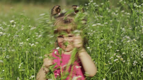 little blonde child girl in pink dress stay on flower chamomile grass meadow. bouquet of daisies