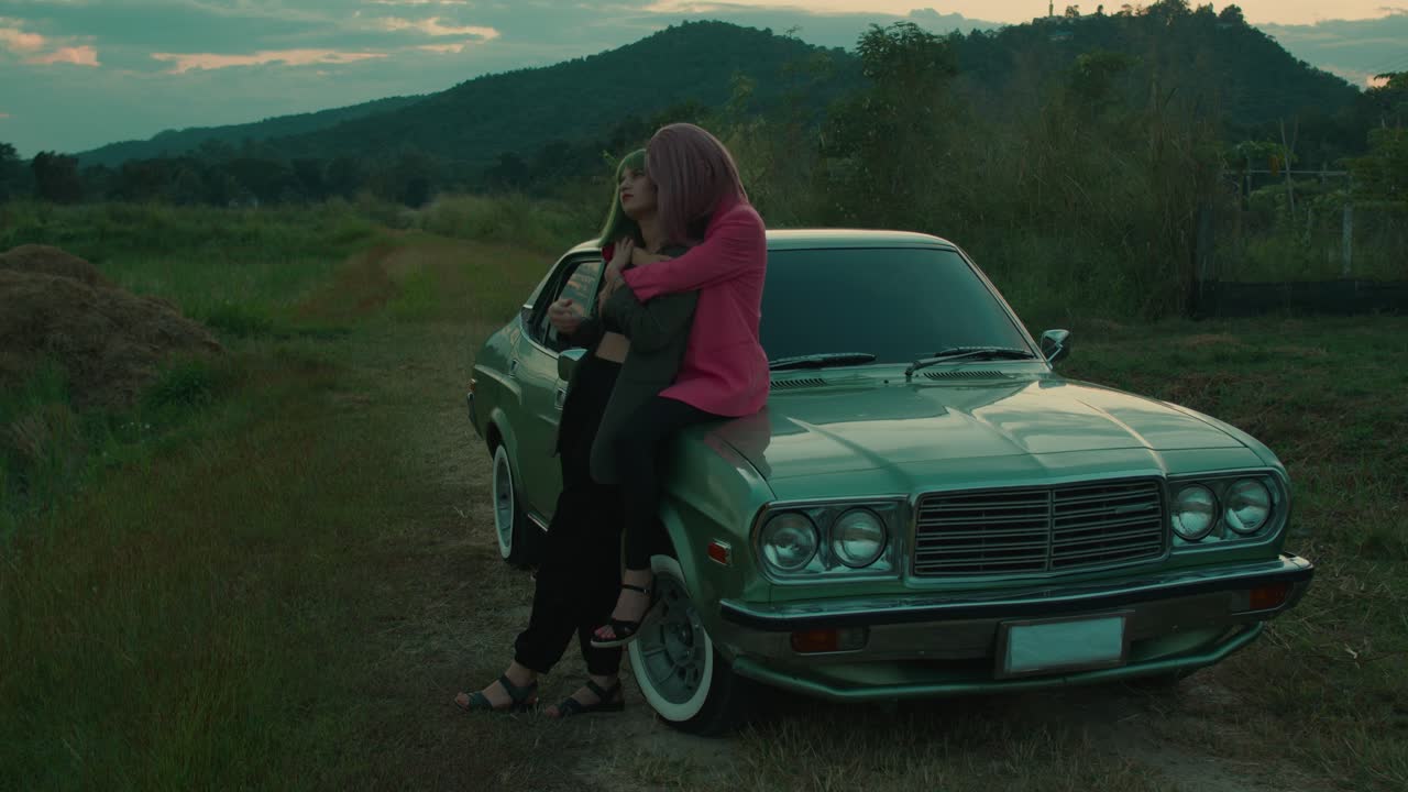 Two women embracing by a vintage car in a countryside setting