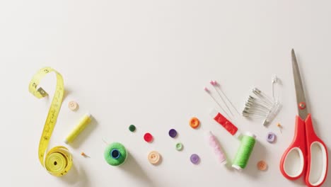 video of scissors, tape measure, buttons, pins and cotton reels on white background with copy space