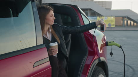 woman taking selfie while charging electric car at airport