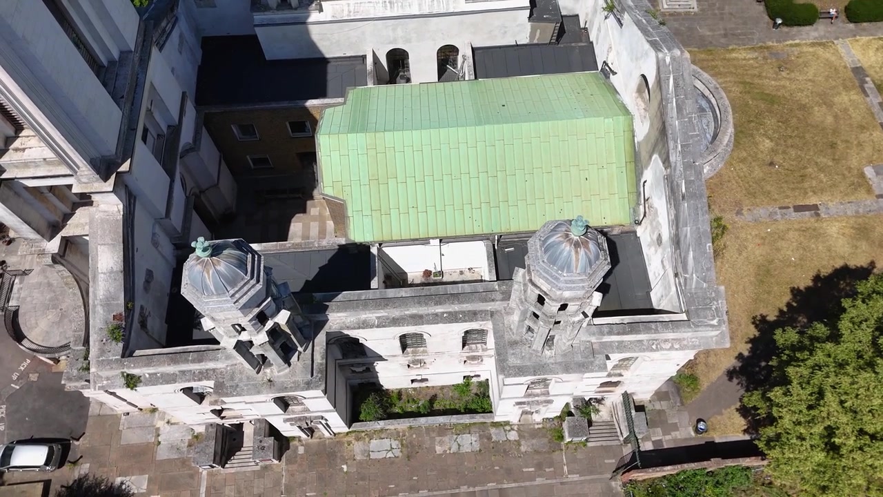Vista de cima de uma igreja barroca com telhado de cobre verde, torres gêmeas e uma torre de pedra branca entre árvores
