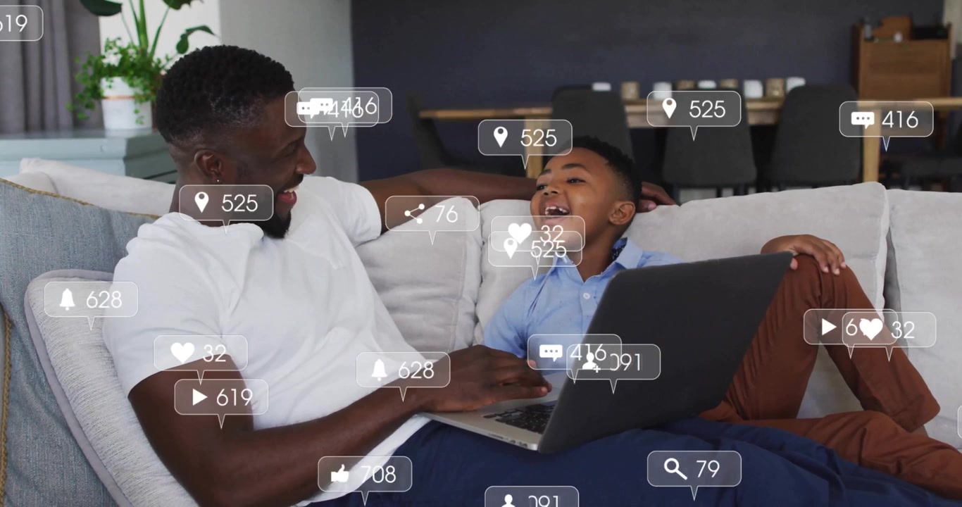 Father and son positioning laptop, typing on sofa creating social media icons showing engagement