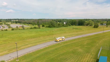 Tiro-De-Drone-De-Un-Camión-De-Bomberos-Amarillo-Conduciendo-A-Través-De-Un-Campo-Verde