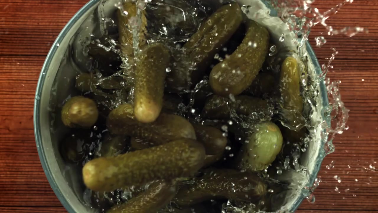 Cornichons tombant dans un bol avec des éclaboussures d'eau au ralenti