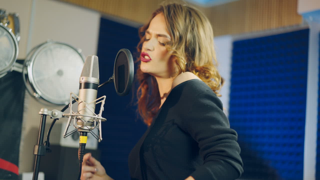 Portrait of a happy female wearing black singing into a modern microphone in audio studio. Side view of a pretty singer and musical equipment