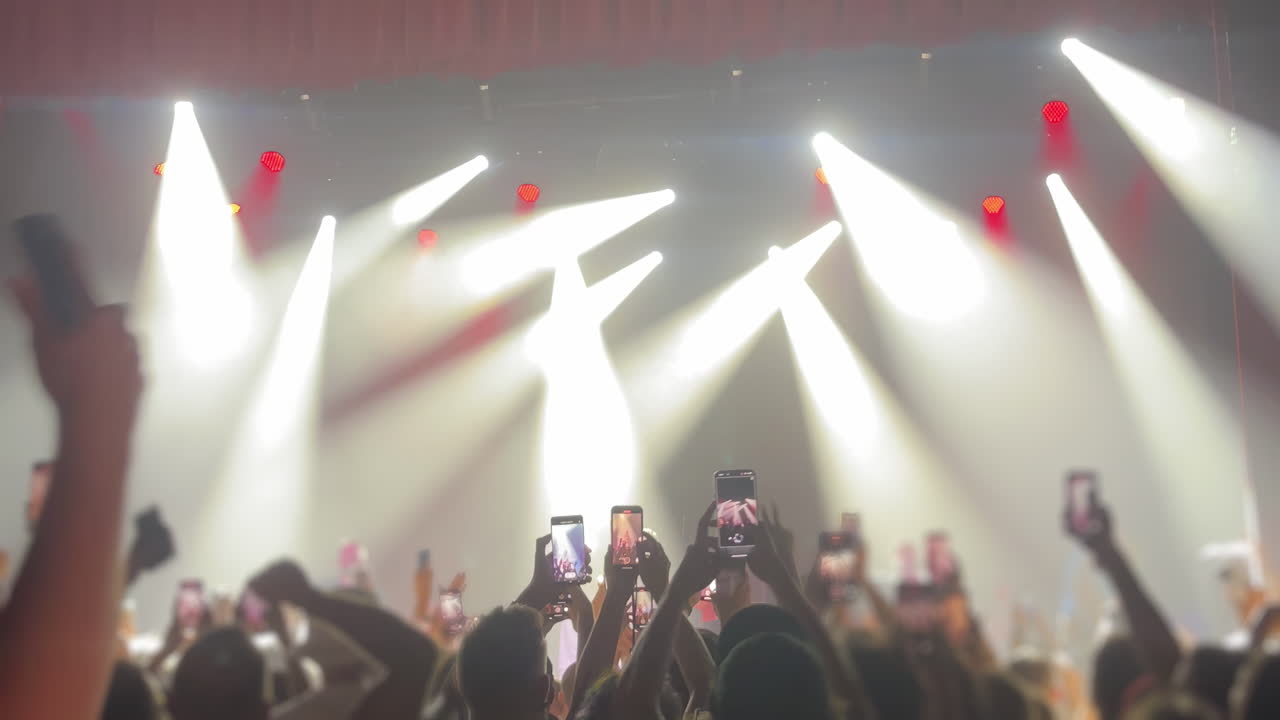 Crowd of concert attendees with raised hands enjoying live music under bright stage lights