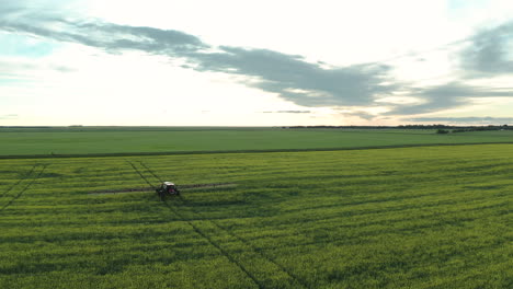 vista aérea escénica de tierras de cultivo verdes y planas expansivas con maquinaria agrícola rociando fungicida en cultivos, saskatchewan, canadá, por encima de la retirada de drones