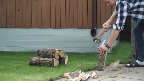 young man with blue checked shirt is chopping wood in smaller pieces