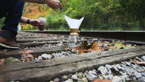 Man-putting-a-scoop-of-blended-coffee-powder-into-a-jar,-kept-on-railway-track