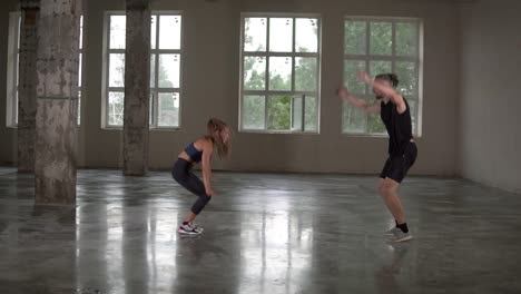 hombre y mujer con dreadlocks en el estudio de fitness haciendo ejercicios juntos, realizando flexiones con saltos y aplausos. interior del loft. vista lateral