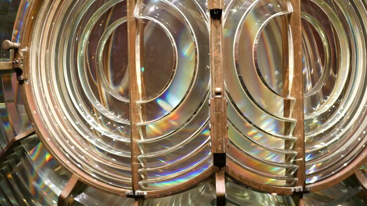 Fresnel lens with brass structure, nautical lighthouse tower. Detail of the glass lantern with rainbow spectrum. System of lamps and lenses to serve as a navigational aid. Old sea searchlight beacon.