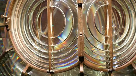 fresnel lens with brass structure, nautical lighthouse tower. detail of the glass lantern with rainbow spectrum. system of lamps and lenses to serve as a navigational aid. old sea searchlight beacon.