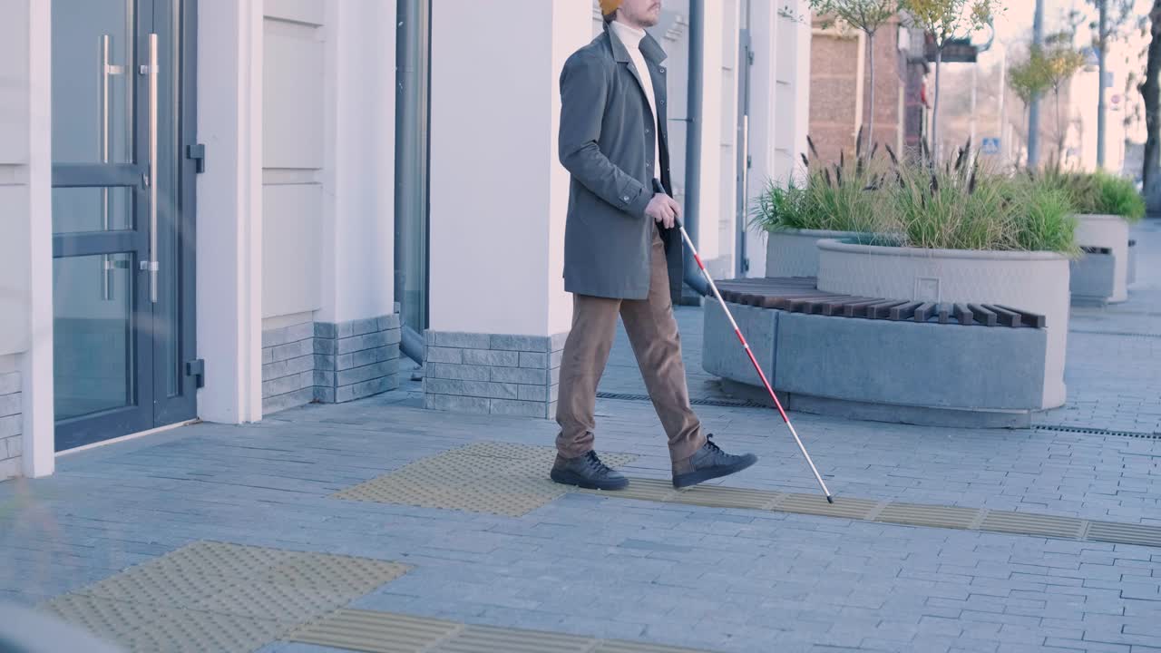 Visually impaired man is walking on a tactile warning tile with the help of his cane. Detectable warning surface for the vision impaired outdoors in the city.