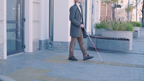 visually impaired man is walking on a tactile warning tile with the help of his cane. detectable warning surface for the vision impaired outdoors in the city.