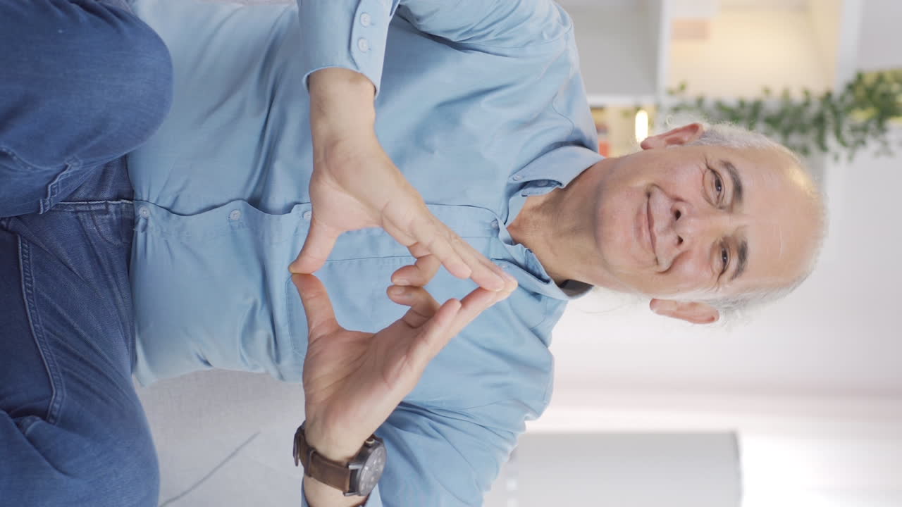 Vertikal video av gammel mann som lager hjertesymbol for kamera