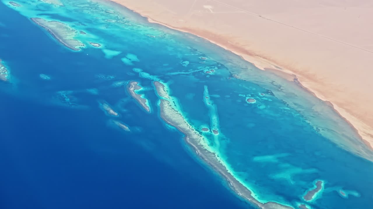 Aerial airplane view over red sea showing brilliant coral reefs and deep ocean blue gradient under sunlight