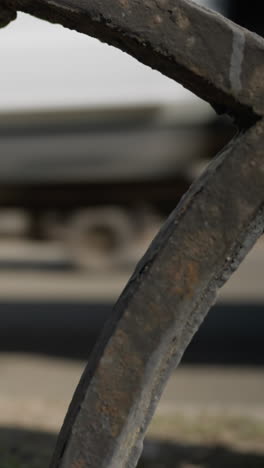 close view of a weathered metal fence with intricate patterns,with cars passing by the road with a blur view of a city building