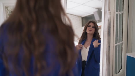 woman tries on elegant blue coat looking in mirror in room