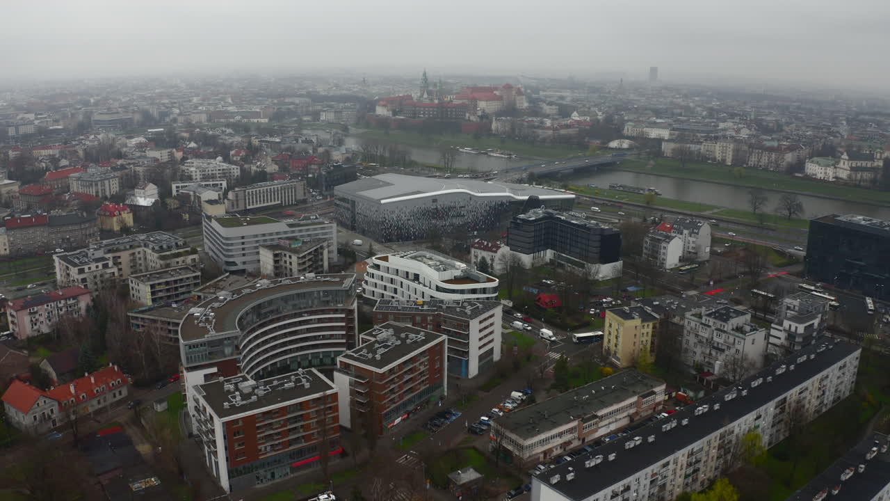 Luftfoto af den tågede by Krakow med Wawel-slottet, Vistula-floden, broer og bygningsværker, der dukker op af tågen på en overskyet dag – bredt panoramaudsnit.
