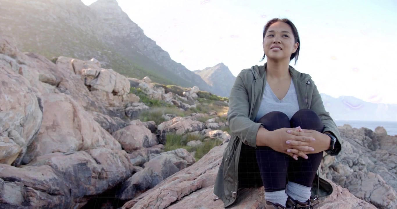 Donna escursionista seduta sulla costa, con cerchi tecnologici dai colori cangianti che emergono intorno alla testa per il tracciamento della meditazione.
