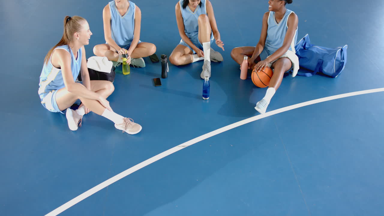 Sitting on basketball court, female players resting and chatting during practice, copy space
