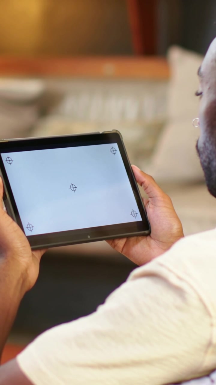 Vertical video: Starting holding tablet, man in light tee adjusting grip on sofa aligning markers