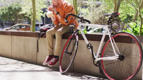 Albino-african-american-man-with-dreadlocks-sitting-in-park-with-bike-eating-sandwich