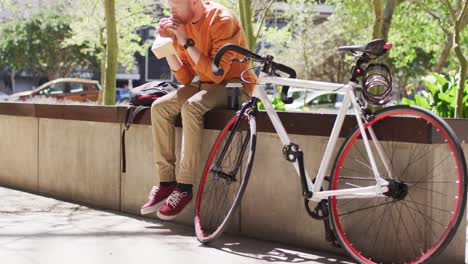 albino african american man with dreadlocks sitting in park with bike eating sandwich