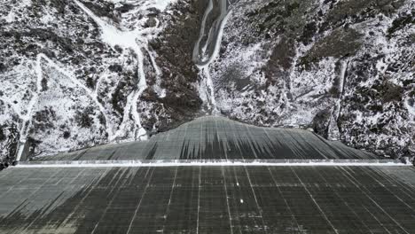 amazing drone footage over an alpine lake, hydro dam and vast alpine reservoir fringed by rugged mountains with a waterside trail after the first snow fall of winter 2022