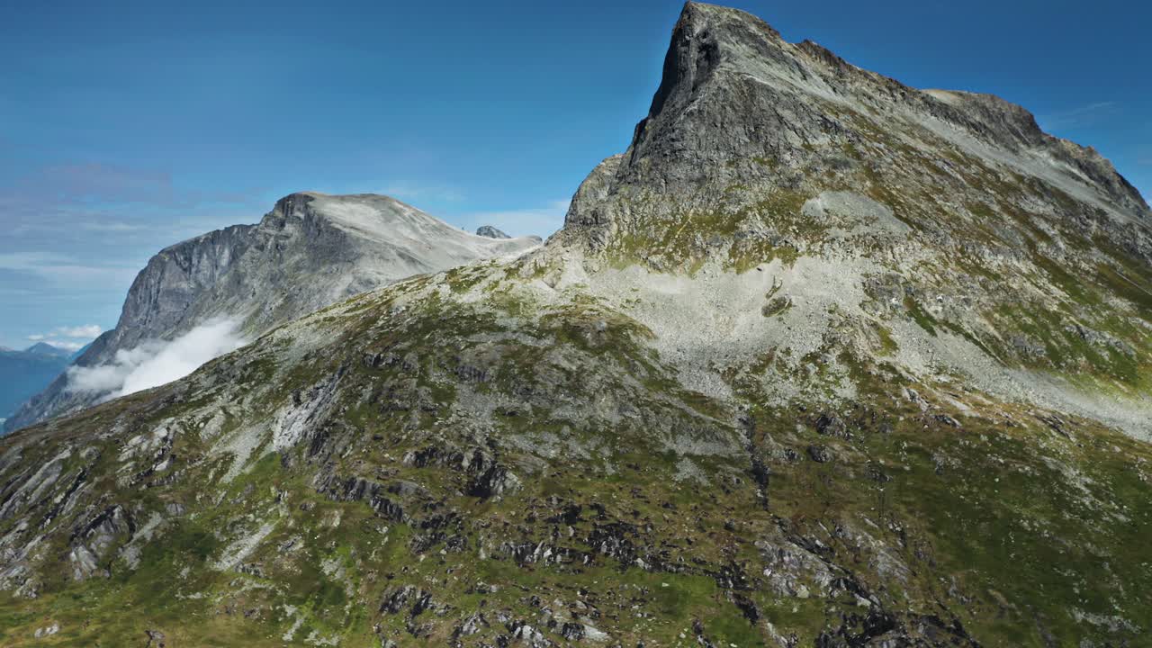 A vast tundra valley with towering mountains, streams, and a small lake. Low clouds whirl between the peaks. An aerial view.
