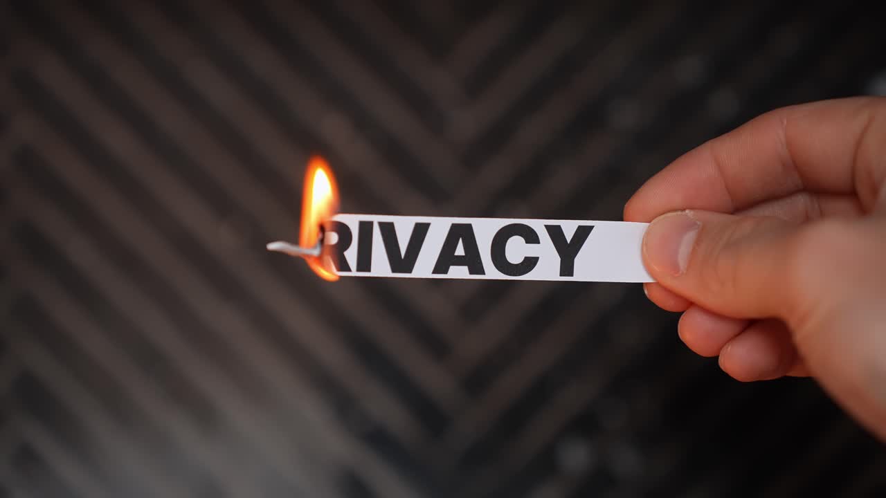 Hand burns a paper label reading “PRIVACY,” symbolizing privacy restored—data protection, security, and regaining control of personal information. Dark background with copy space